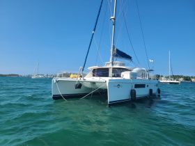 A stunning catamaran named 'Friend Ship' anchored in clear blue waters, showcasing its sleek design against a vibrant coastal backdrop.