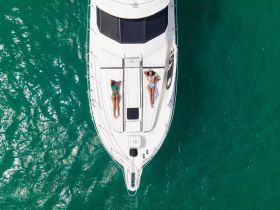 Two friends relax and sunbathe on the deck of a luxurious yacht, surrounded by sparkling turquoise waters — a perfect summer getaway.