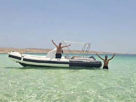 Two friends celebrate in the shallow waters next to their boat, enjoying a sunny day at the beach — perfect for summer adventures and fun on the water.