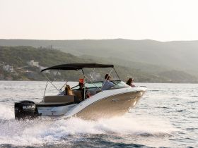 A group enjoys a thrilling ride on a speedboat, cutting through the waves against a scenic backdrop of hills and coastal homes — perfect for adventure seekers on the water.
