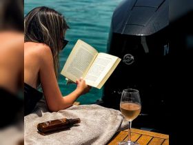 A woman enjoys a relaxing day on the water, reading a book and sipping wine, with the boat's motor visible in the background — perfect for unwinding on a sunny day.