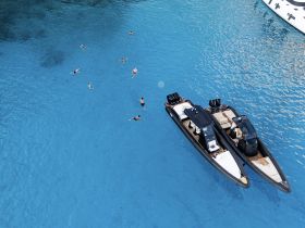 A vibrant scene of swimmers enjoying the crystal-clear turquoise waters near two boats, perfect for a fun day on the water with friends.