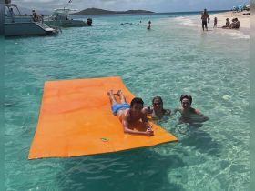 A fun day at the beach with friends enjoying a floating mat in crystal-clear waters — perfect for relaxation and summer adventures.