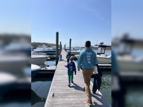 A family walks along the dock towards their boat, enjoying a sunny day by the water — a perfect start to a boating adventure.