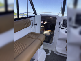 Interior view of a boat cabin showcasing comfortable seating and access to the restroom area, perfect for relaxing during a day on the water.