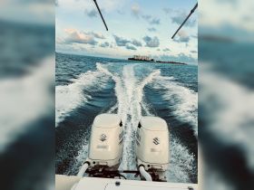 A view from the back of a boat showcasing twin Suzuki outboard motors as it cruises through open waters, leaving a wake behind.