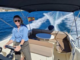 A woman confidently steers the boat from the helm, showcasing the comfortable interior seating and the vibrant blue waters behind her — perfect for a day of adventure on the water.