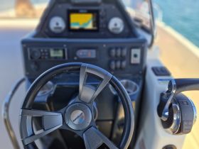 A close-up view of the helm and console of a boat, showcasing the steering wheel and navigation equipment, ideal for understanding boat controls and features.