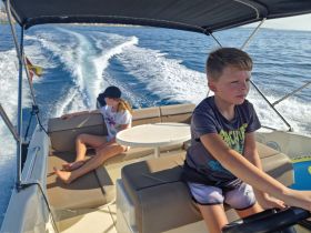 Two children enjoy a sunny day on a boat, with one steering while the other relaxes — a perfect snapshot of family fun on the water.