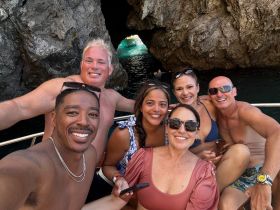 A cheerful group of friends enjoys a fun day on the water, capturing memories with a selfie near a stunning cave backdrop — perfect for snorkeling adventures.