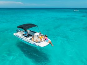 A lively group enjoys a sunny day on the water aboard a rental boat, showcasing the perfect setting for fun and relaxation in crystal-clear turquoise waters.