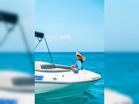 A joyful woman enjoys a sunny day on a boat, sipping a drink while surrounded by the beautiful ocean — perfect for a relaxing getaway.