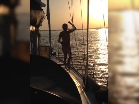 A silhouetted figure enjoys a sunset while sailing, capturing the essence of adventure on the water.