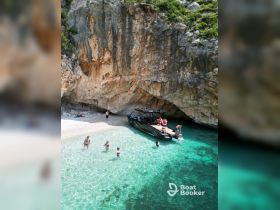 A lively group enjoys a refreshing swim in crystal-clear waters near a stunning beach, with a sleek boat anchored nearby — perfect for a fun day on the water.