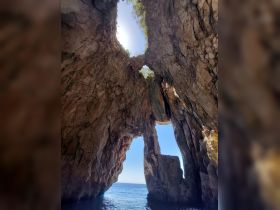 A stunning view of a natural rock formation with a hole, showcasing the beauty of the coastline — a perfect spot for sightseeing and exploration during boat tours.