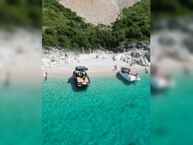 A vibrant scene at a secluded beach with two boats anchored, where guests enjoy swimming and relaxing in the crystal-clear turquoise waters — a perfect getaway for summer adventures.