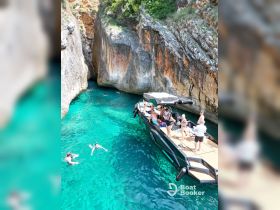 A lively group enjoys a refreshing swim in a stunning cove, with a sleek boat anchored nearby — perfect for summer adventures and water activities.