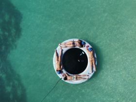 A group of friends relaxes on a floating mat in crystal-clear waters, enjoying a perfect day of sunbathing and swimming.