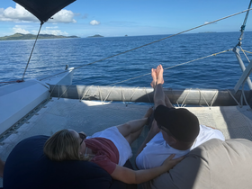 A couple relaxes on the deck of a catamaran, enjoying the serene ocean view and distant islands — a perfect moment for romance and tranquility on the water.