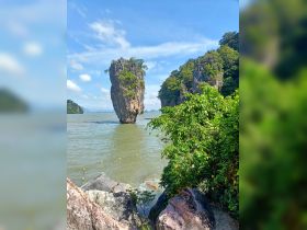 A stunning view of a unique limestone rock formation surrounded by lush greenery and calm waters, perfect for exploring scenic coastal landmarks.
