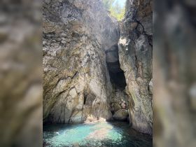 A stunning view of a rocky cave with clear turquoise water, featuring a person exploring the natural beauty — perfect for adventure seekers and nature lovers.