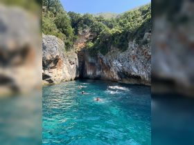 A group of swimmers enjoys the crystal-clear waters of a secluded cove, surrounded by stunning rocky cliffs and lush greenery — a perfect spot for adventure and relaxation.
