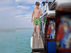 A young boy steps off a boat into the clear waters, capturing the joy of summer adventures on the water.
