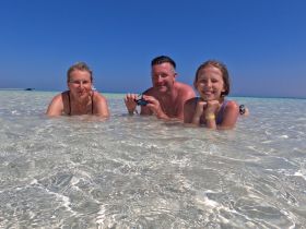 A joyful family enjoys a sunny day swimming in crystal-clear waters, capturing a perfect moment of fun and togetherness at the beach.