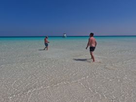 Two men enjoy a sunny day wading in the crystal-clear waters of a beautiful beach, perfect for relaxation and fun in the sun.