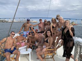 A lively group of friends enjoys a fun day on a yacht, celebrating with drinks and laughter against a scenic backdrop.