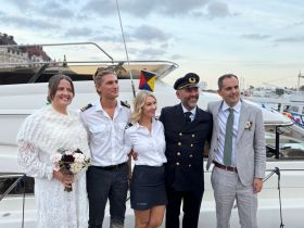 A joyful group poses for a photo on a boat, celebrating a wedding occasion. The festive atmosphere highlights the perfect backdrop for memorable moments on the water.