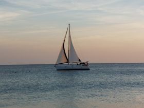A serene view of a sailboat gracefully sailing on calm waters during sunset, perfect for showcasing tranquil boating experiences.