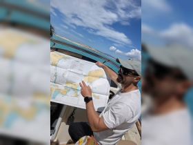 A man enthusiastically discusses navigation while holding a map on a boat, showcasing the excitement of planning a maritime adventure on the open ocean.