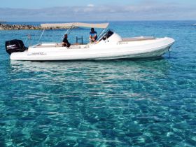 A sleek boat glides through crystal-clear waters with two individuals on board, showcasing the perfect setting for a day of adventure on the sea.