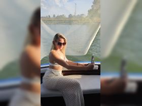 A young woman enjoys a sunny day on the boat, capturing a selfie while relaxing by the water — perfect for social media moments on a boating adventure.