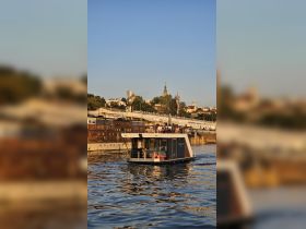 A stylish boat navigates the river with guests enjoying the view, set against a vibrant cityscape — perfect for leisurely outings and sightseeing.