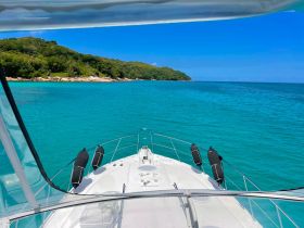 A stunning view from the front of a yacht, showcasing the vibrant turquoise waters and lush greenery of the coastline — perfect for a serene day on the water.