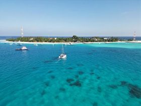 A stunning aerial view of a sailboat navigating through crystal-clear turquoise waters, with a picturesque island in the background — a perfect representation of tropical paradise.