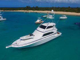 A stunning aerial view of a luxurious yacht anchored in clear turquoise waters, surrounded by other boats and a sandy beach, perfect for a day of relaxation and adventure.