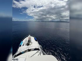 A stunning view from the front of a yacht cruising through calm waters, showcasing the beautiful horizon and clear skies — perfect for a day on the water.