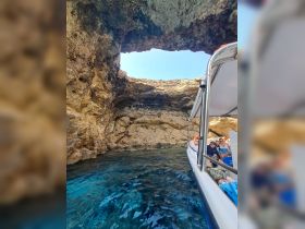 A scenic view from inside a cave with a boat and guests enjoying the stunning surroundings — perfect for exploring hidden gems on the water.