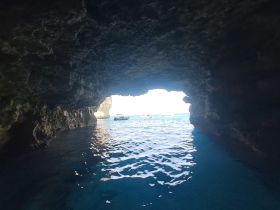 A stunning view from inside a cave looking out towards the sea, with a boat visible in the distance — a perfect representation of coastal exploration and adventure.
