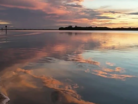 A stunning sunset casts vibrant colors over the calm waters, creating a picturesque reflection along the coastline — perfect for serene evening boat trips.