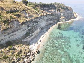 A stunning aerial view of a beach with clear turquoise waters and rocky cliffs, showcasing a perfect destination for sunbathing and relaxation.