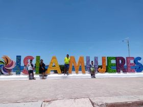 A group of visitors poses in front of the colorful Isla Mujeres sign, capturing a memorable moment at this iconic landmark.