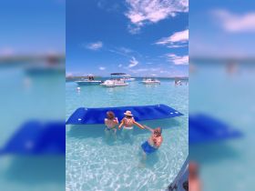 A fun day in the water with friends enjoying a floating mat, surrounded by boats in a beautiful turquoise setting — perfect for summer gatherings and water activities.