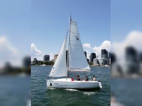 A group of friends enjoys a sailing adventure on the 'HotFlash' in front of a stunning city skyline, perfect for summer outings on the water.