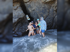 A fun group of friends poses in the water near a rocky formation, capturing a memorable beach day filled with laughter and adventure.