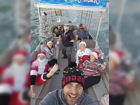 A festive group celebrates the holiday season aboard a pontoon boat, complete with Christmas decorations and drinks, making for a fun and memorable outing on the water.