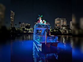 A beautifully decorated charter boat, 'Beach Bum Charters,' illuminated with festive lights at night, creating a vibrant atmosphere on the water.